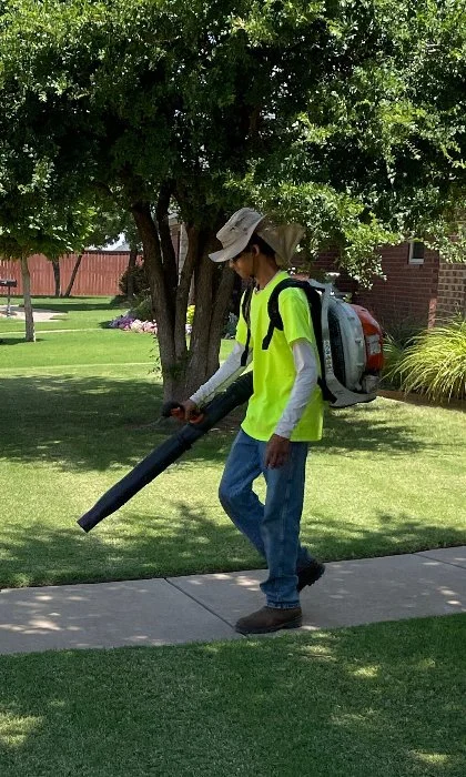 Crew member performing lawn maintenance services to blow debris from sidewalks..
