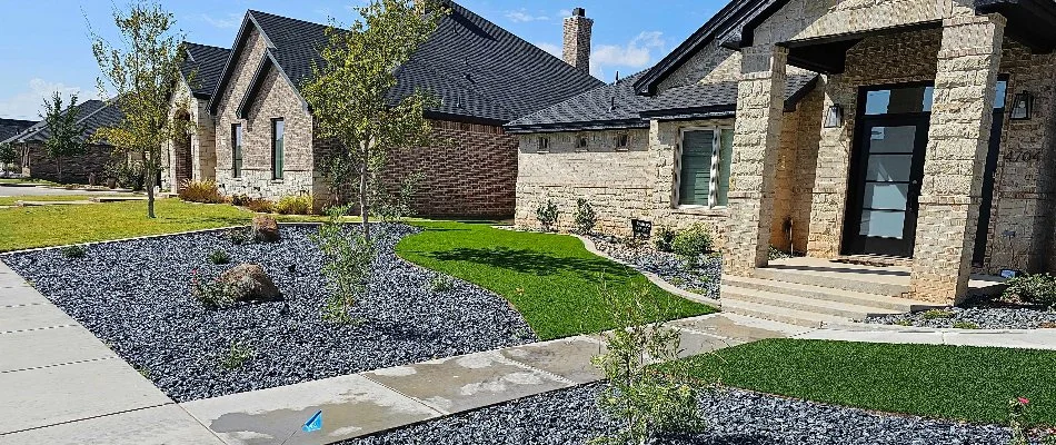 House in New Home, TX, with green lawn, landscaping rocks, and trees.